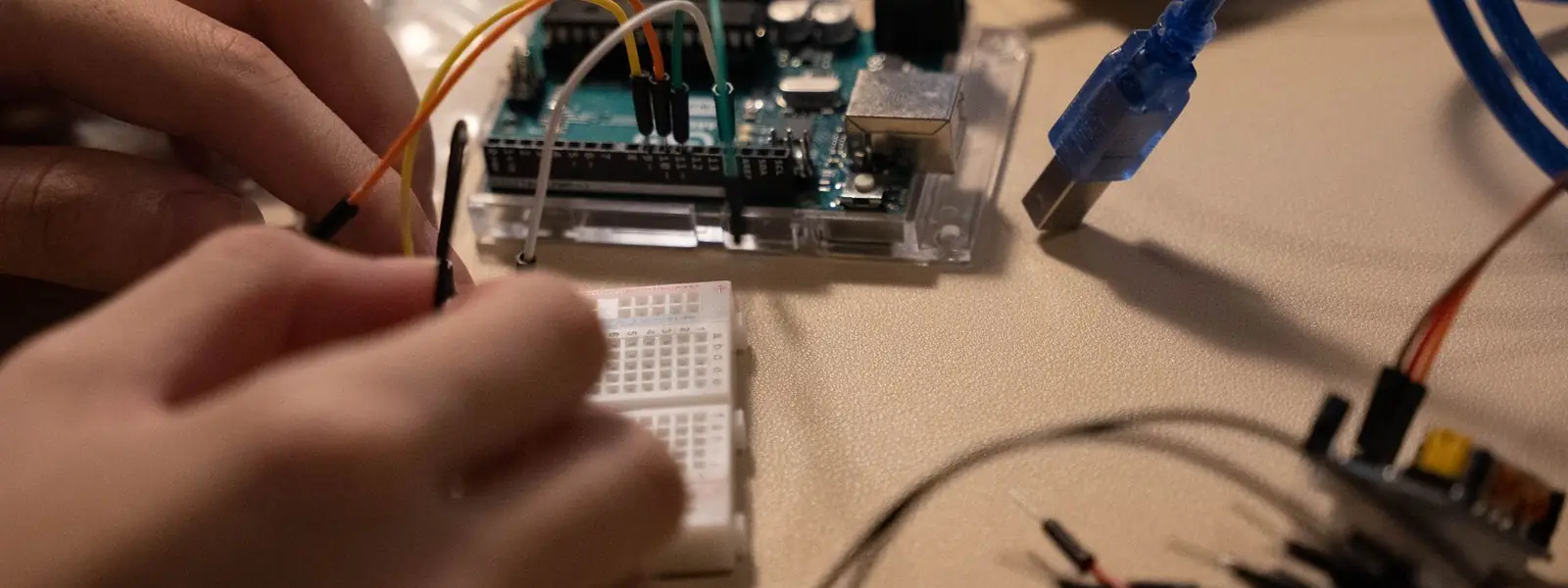 Two hands wiring a microcontroller board to a breadboard with jumper leads.