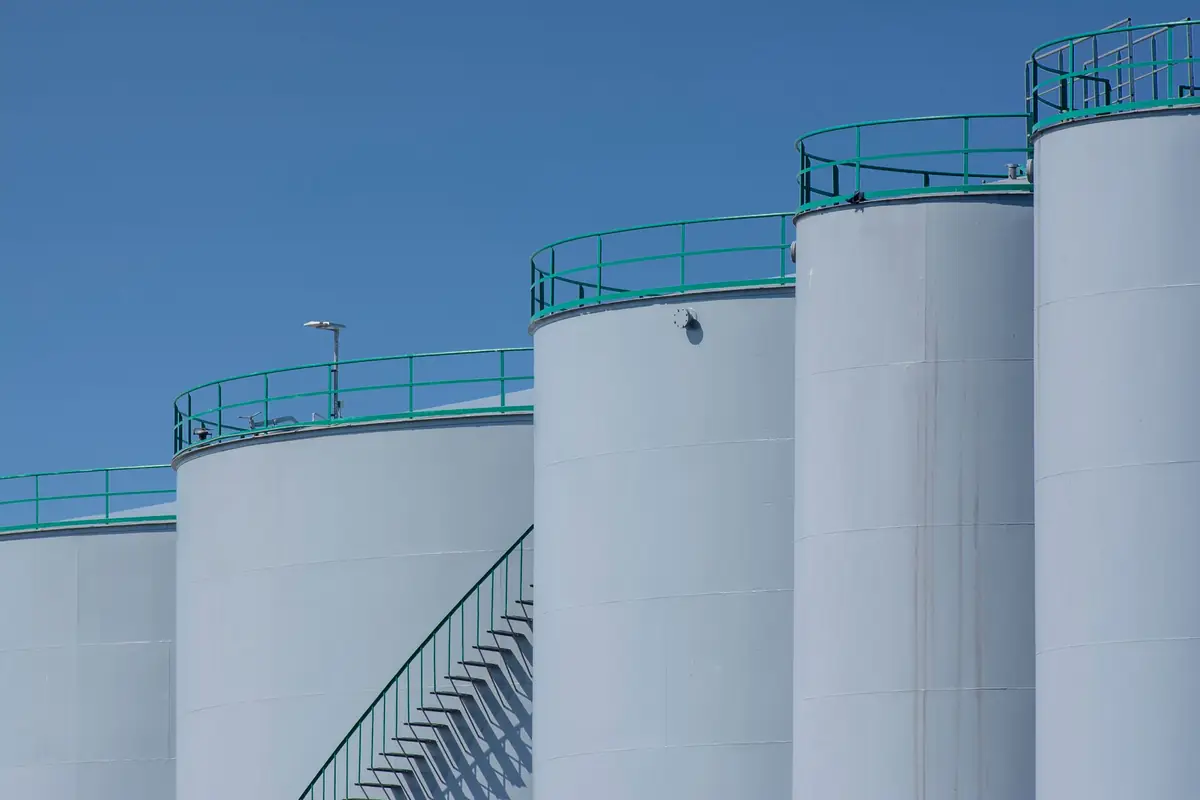 A row of tall industrial storage tanks with external stairs and walkways.